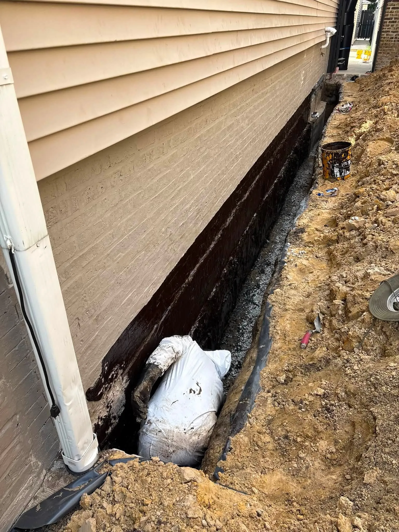 Rubberised waterproofing membrane being applied to a foundation wall in an open trench in Etobicoke